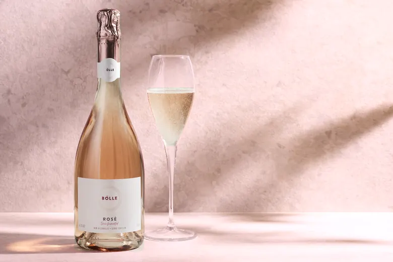 Flaska af BOLLE Sparkling Rosé og fullt glas við ljósan vegg